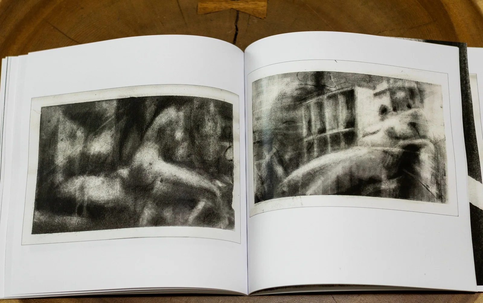 Inner Body – Open Spread Inner Body somatic sketchbook open on a wooden table, showing two dark charcoal figure drawings